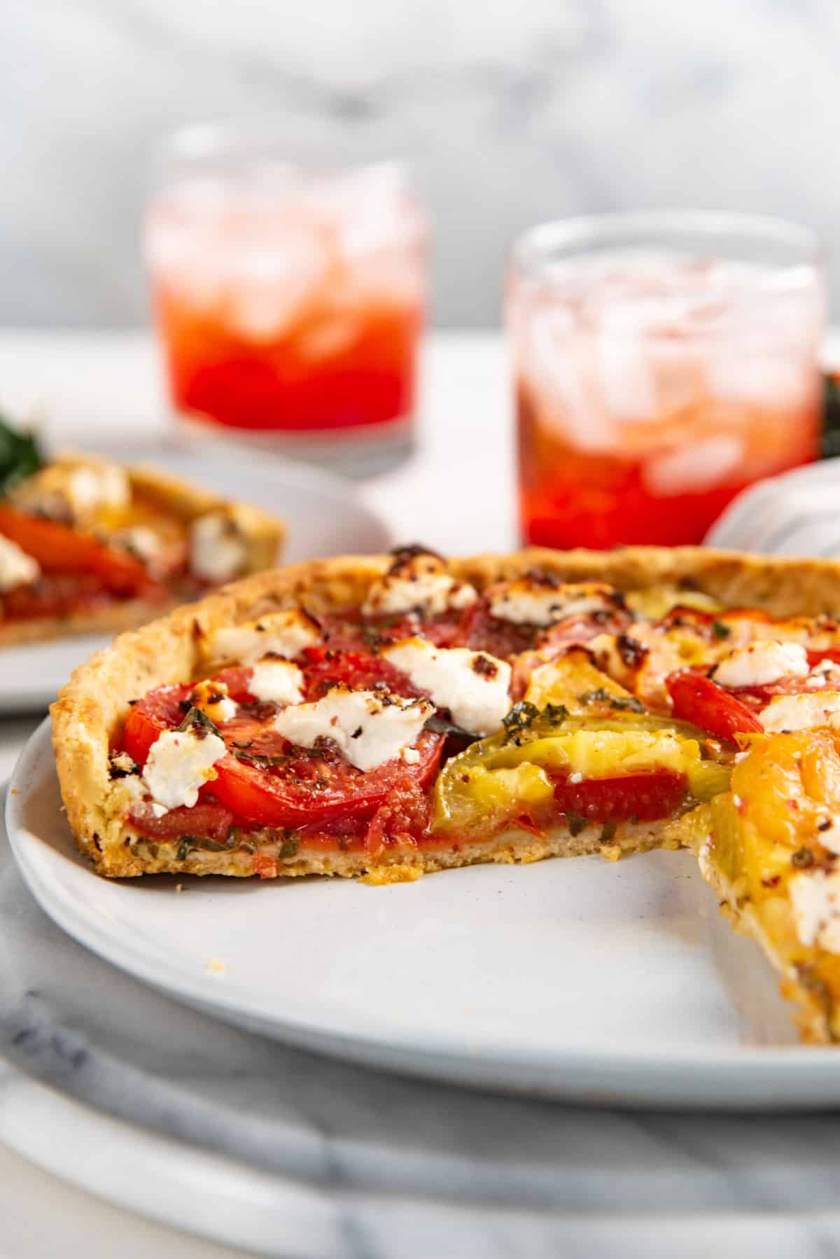 Close up of a tomato tart with a slice cut out to show a cross section of the tart crust and the tart layers.