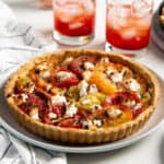Fresh tomato tart with caramelized heirloom tomato slices and cheese, and golden brown tart crust served on a white plate.