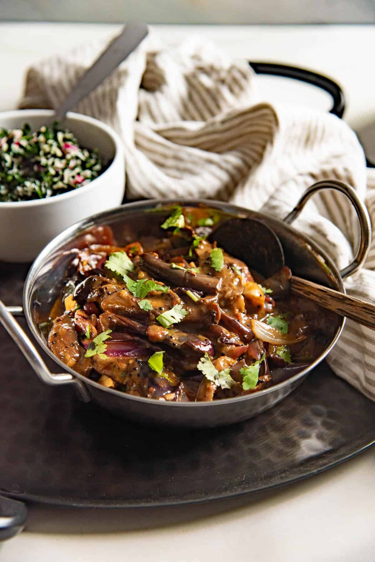 South Asian brinjal curry (aubergine curry) served in a small saucepan with a wooden spoon.