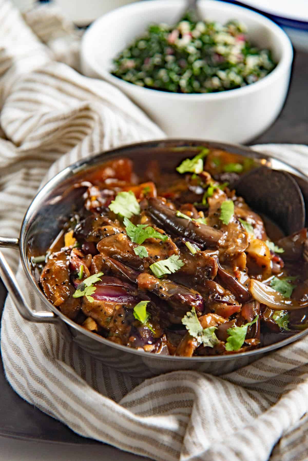 Close up of the eggplant curry in a stainless steel saucepan. It's topped with chopped cilantro.