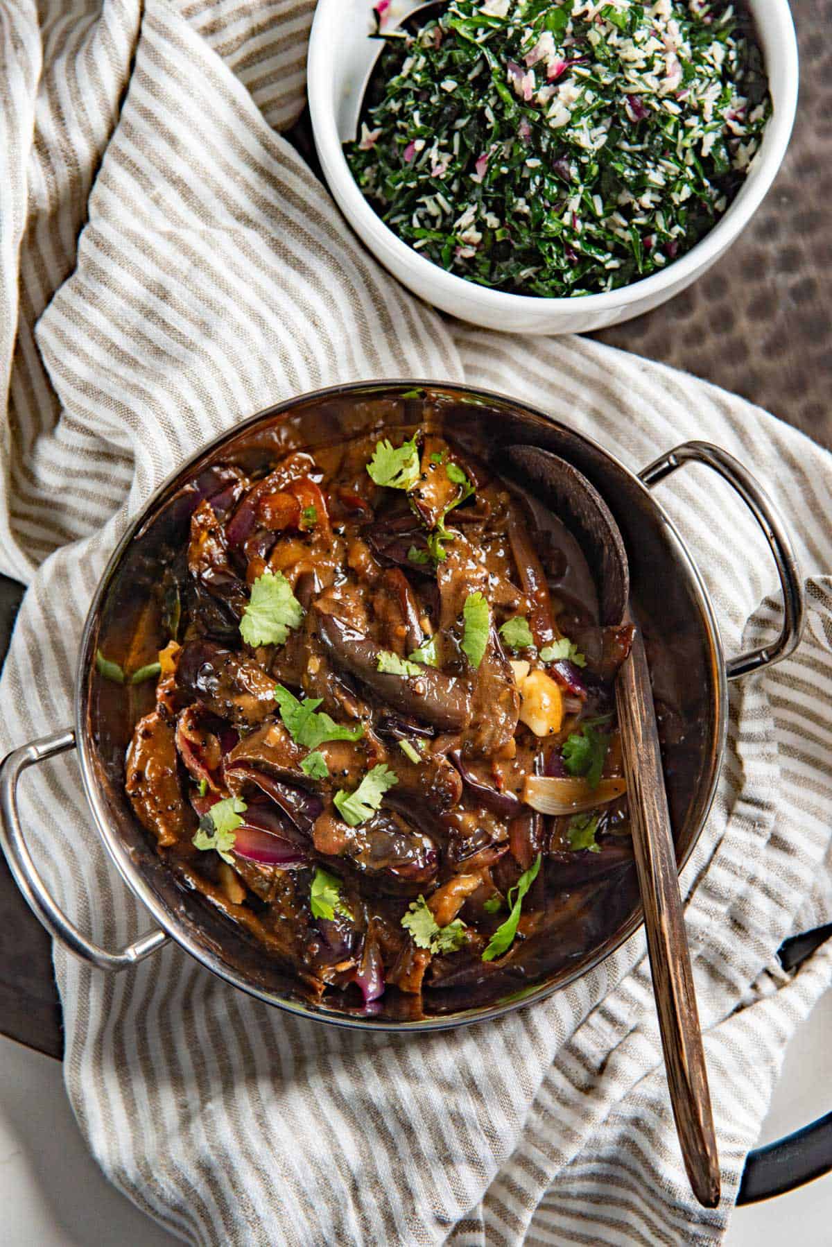 Overhead view of the eggplant curry and curry base served in a small saucepan with a wooden spoon.