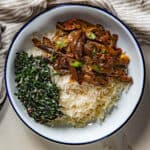 Eggplant curry served in a white plate with white rice and a green salad.