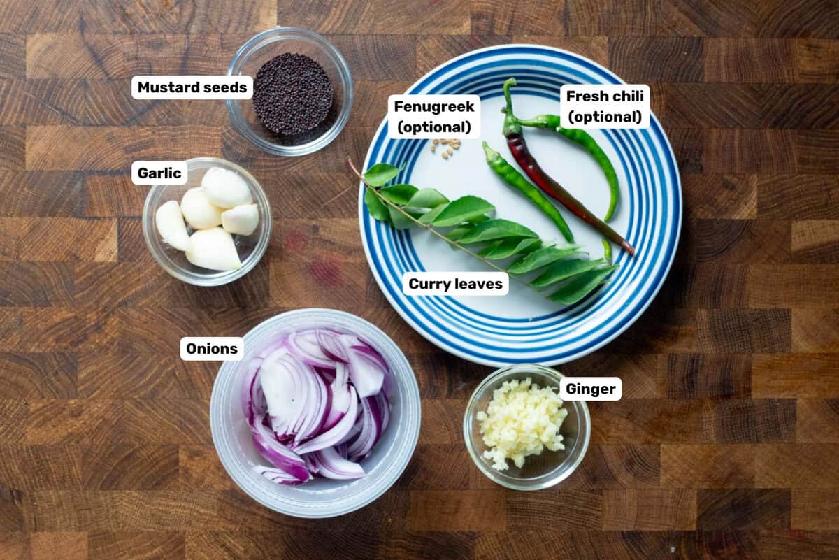 Labeled ingredients needed to temper (a technique called tadka) the brinjal curry placed on a wooden surface.