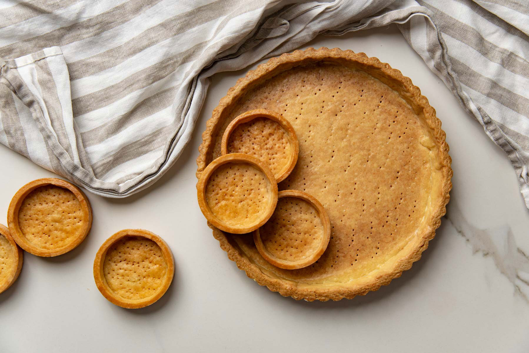 Golden brown tart crusts made with French shortcrust pastry on a white surface.