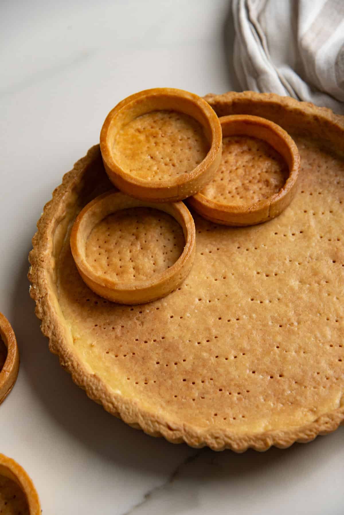 Close up of a large tart crust and three mini tarts after blind baking. They are golden brown and perfectly shaped.