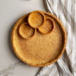 Overhead view of a large pâte brisée tart crust and several mini tarts on a white surface. They are golden brown after being blind baked.
