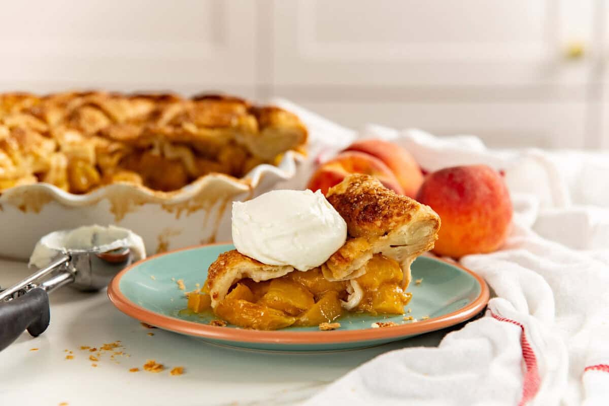 Close up of a peach pie slice on a plate with a dollop of whipped cream on top.