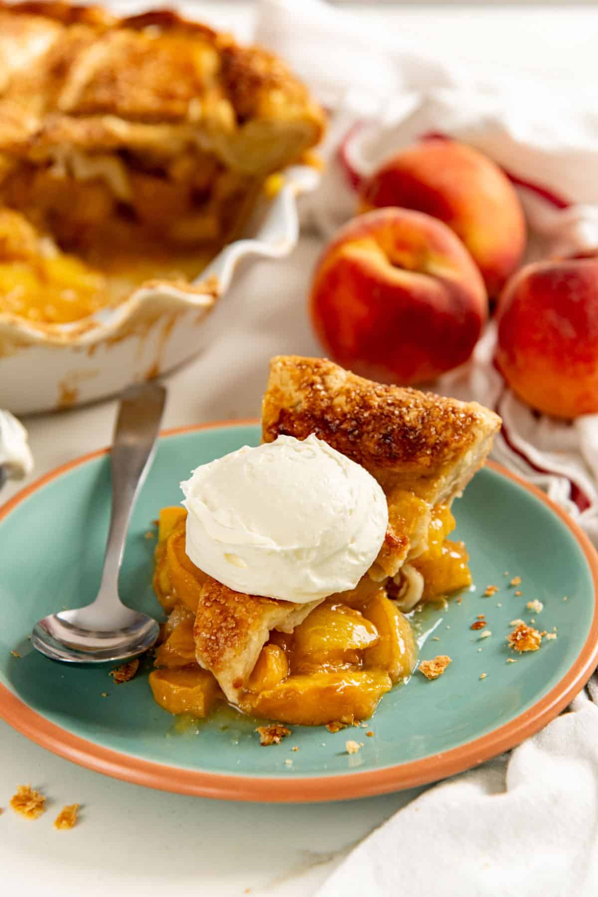 Peach pie slice served on a small green plate with a spoon and whipped cream.