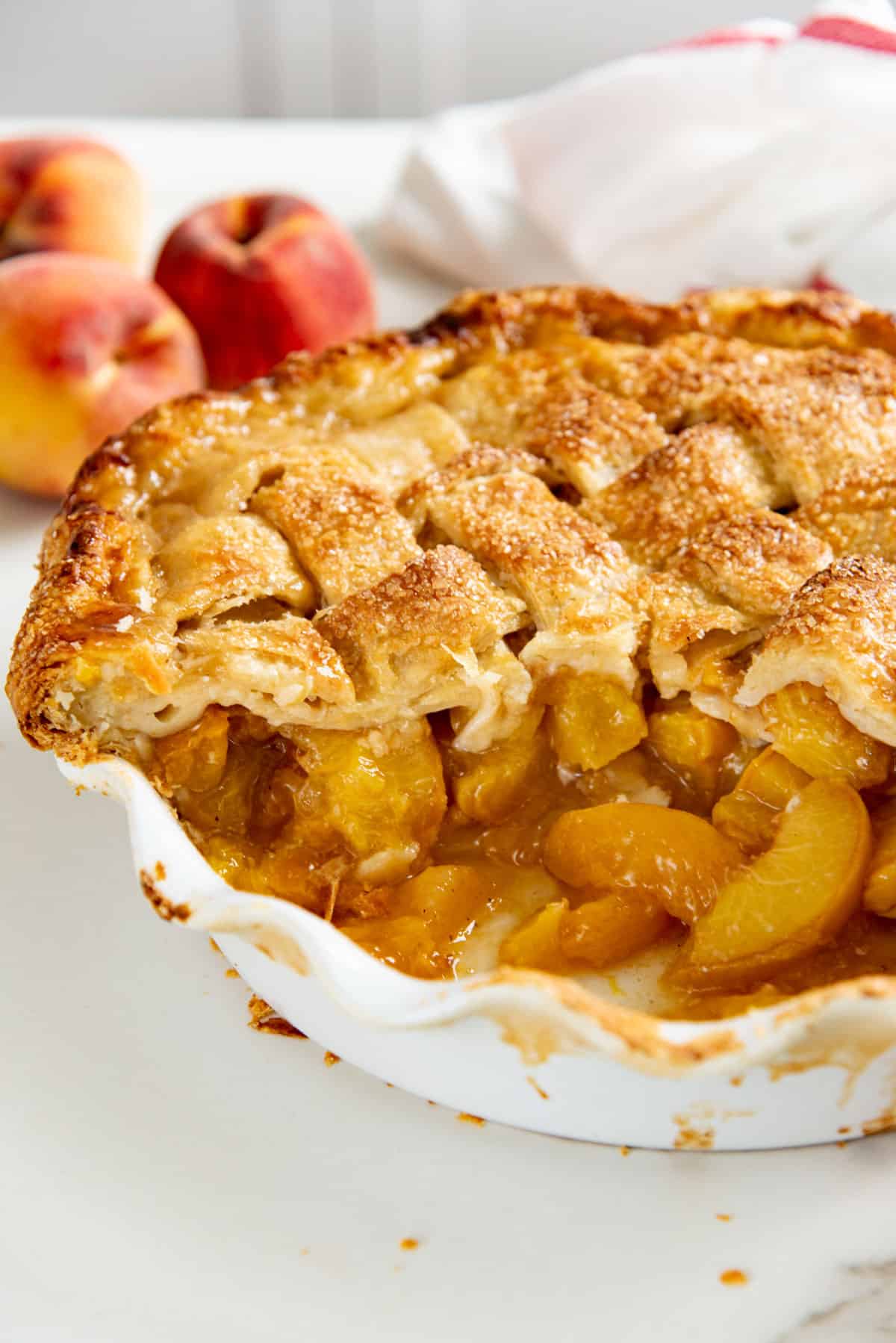 Peach pie with a golden lattice crust in a deep pie dish, with a large piece taken out to show the juicy peach filling inside.